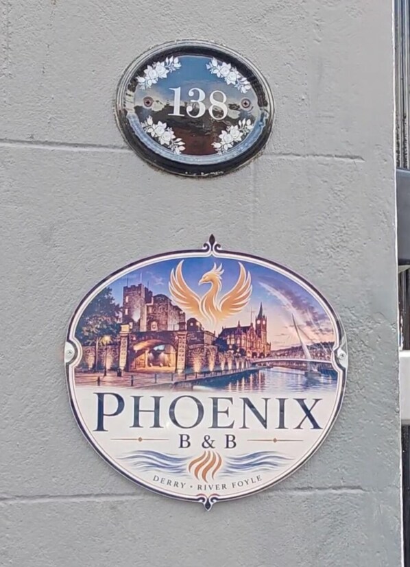 Una placa con número de casa y un letrero de Phoenix B&B con la imagen de un pájaro y un castillo.
