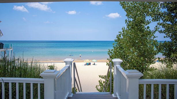 A beach view from a porch with a railing, clear sky, and calm sea.