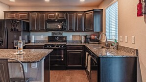 A modern kitchen with dark cabinetry, granite countertops, a stainless steel refrigerator, a microwave, a stove, and a dishwasher.