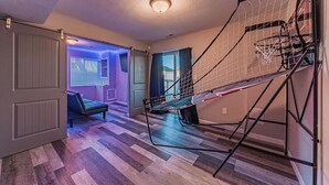 A room with a basketball hoop, a door, a bench, and a window with curtains.