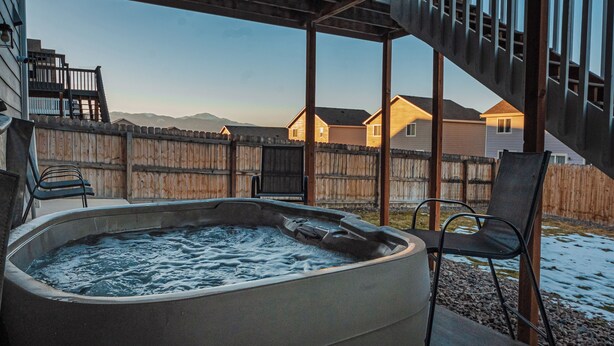 A hot tub under a wooden deck with a view of houses and mountains.