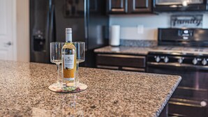 A kitchen with a granite countertop, a bottle of wine, and glasses on a coaster.