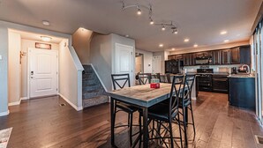 A modern kitchen with dark cabinetry, a wooden dining table, and a staircase leading to another level.