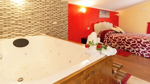 Una habitación con una bañera, una cama con colcha de cuadros rojos y blancos, y una pared roja con una lámpara.