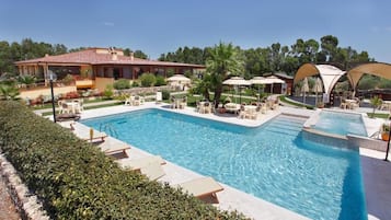 Una piscina con sillas de descanso, sombrillas y un edificio al fondo.
