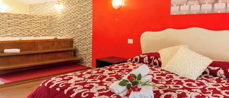 Une chambre d’hôtel avec un mur rouge, un banc en bois, un lit recouvert d’une courtepointe à motifs rouges et blancs, et un tableau représentant des pierres.