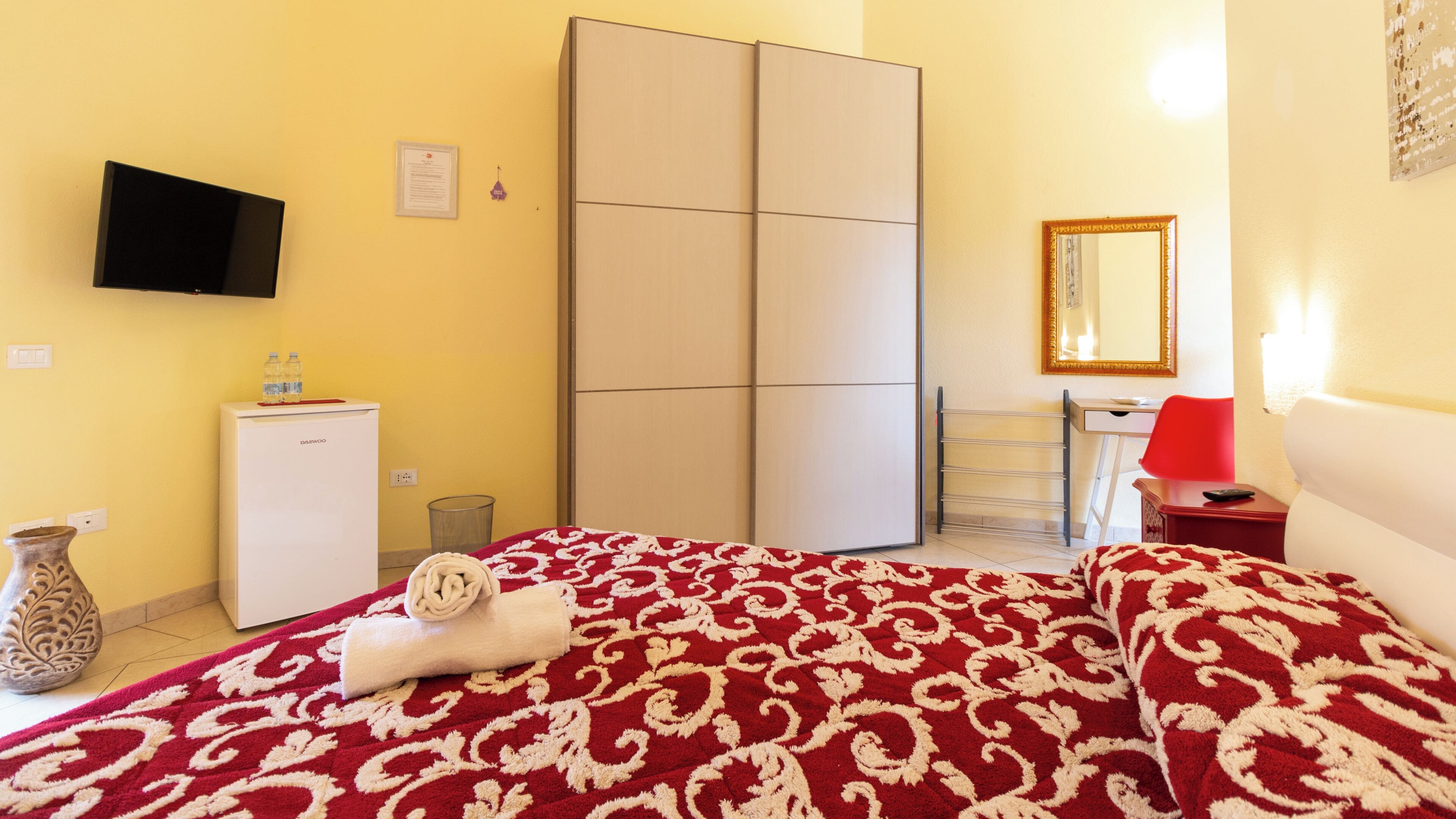 A hotel room with a bed, a desk, a wardrobe, a television, and a mirror.