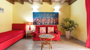 Una habitación con un sofá rojo, una mesita con revistas, un sillón rojo, una planta en maceta y un cuadro de flamencos en la pared.