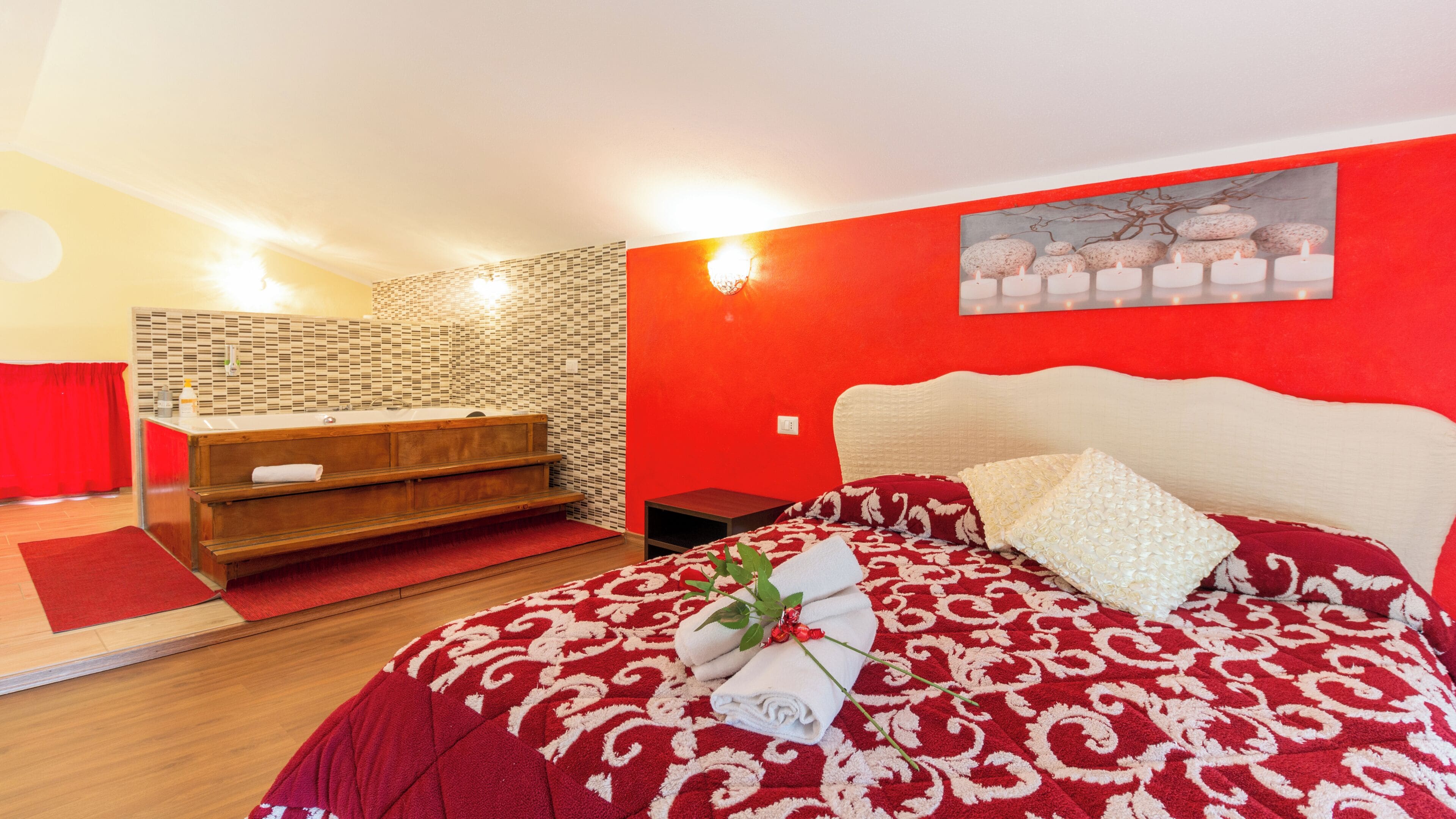 Un dormitorio con pared roja, un banco de madera, una cama con colcha de cuadros rojos y blancos, y una lámpara de pared.
