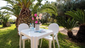 Juego de mesa y sillas de plástico blanco al aire libre, con una palmera y flores al fondo.
