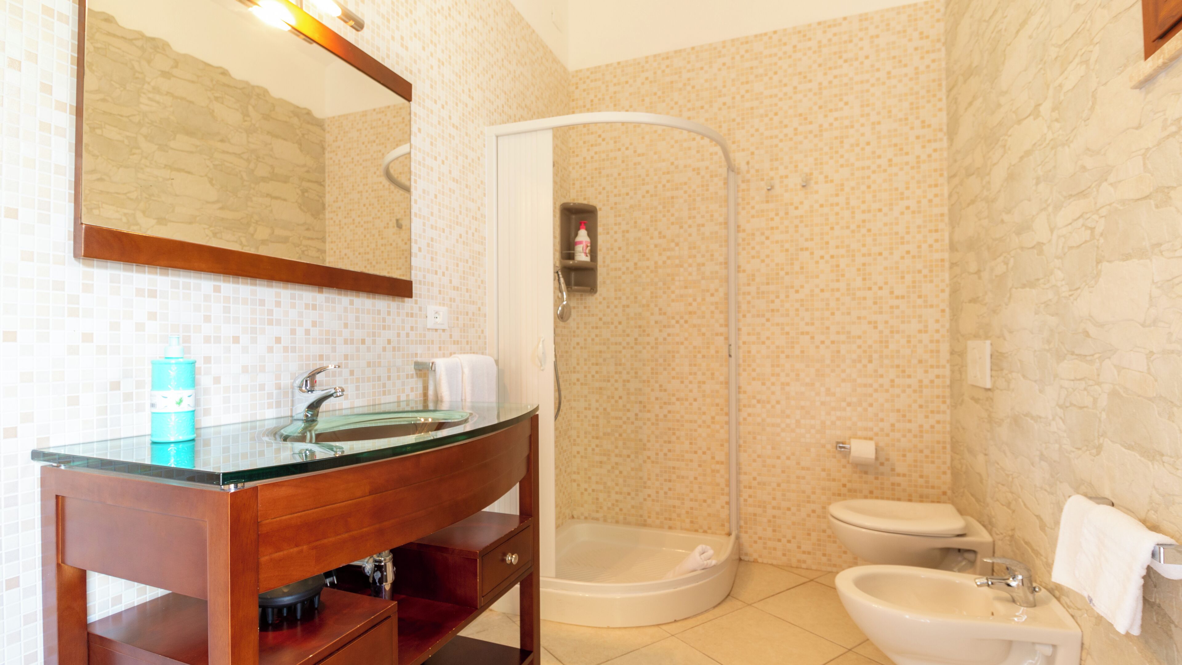 A bathroom with a glass sink, a shower, and a toilet.