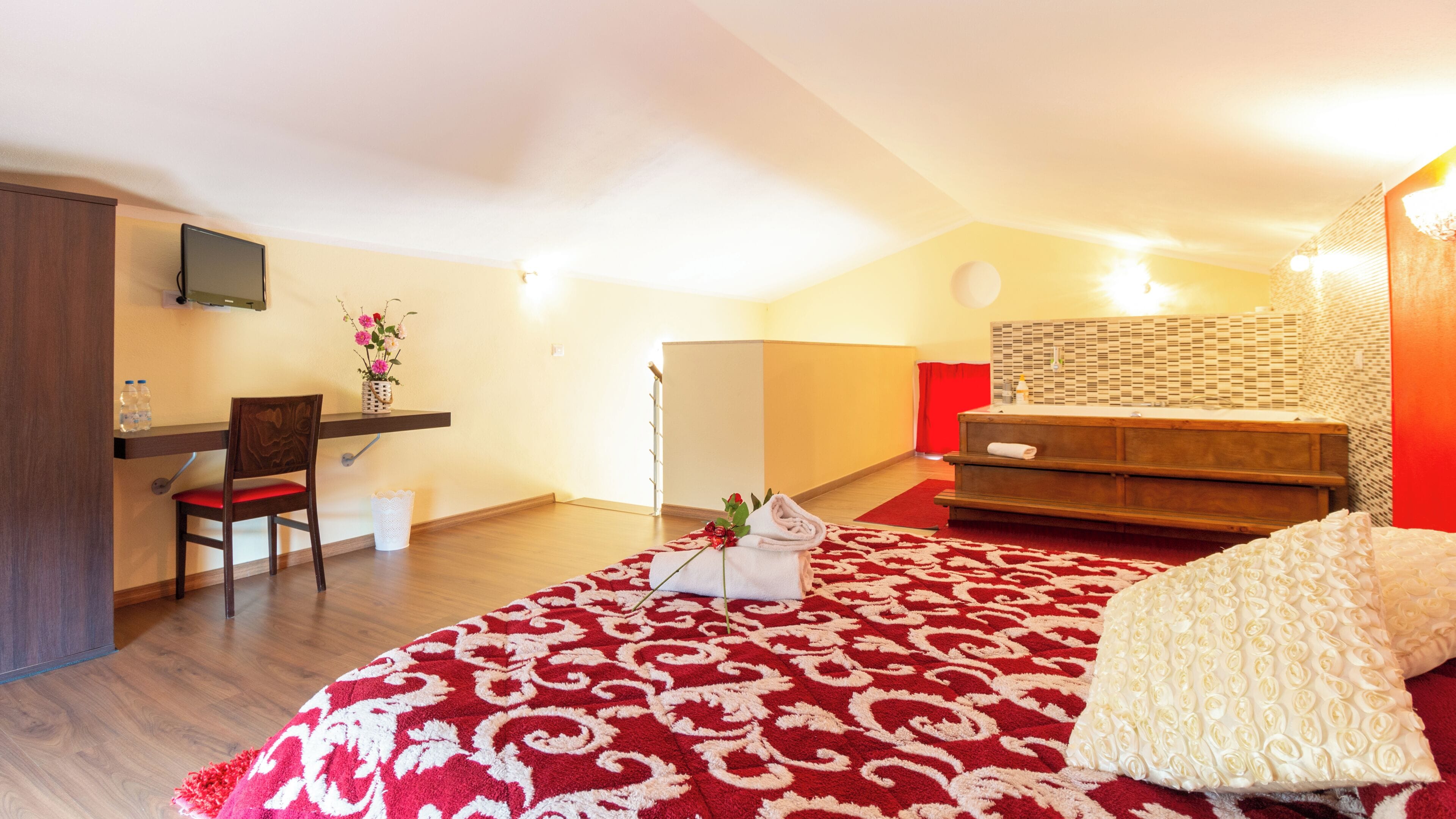 Une chambre à coucher comprenant un lit, un bureau, une chaise, une petite table avec un vase de fleurs, et une salle de bain avec un rideau de douche.