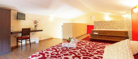 A bedroom with a bed, a desk, a chair, a small table with a vase of flowers, and a bathroom with a shower curtain.