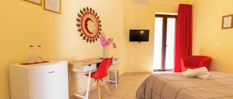 A hotel room with a bed, a desk with a chair, a refrigerator, a TV, and a window with curtains.