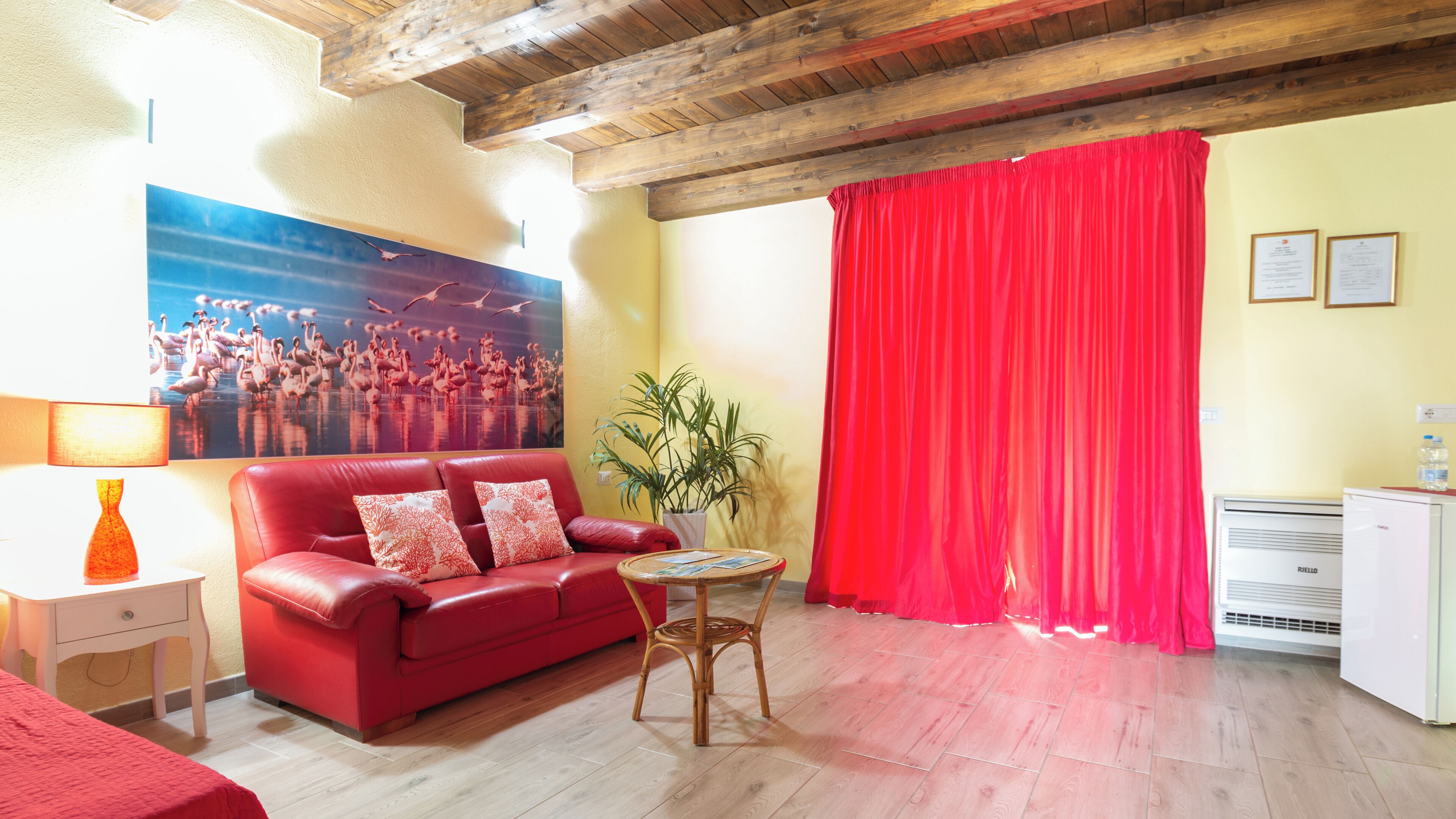 Una habitación con un sofá rojo, una mesita, una planta en maceta, una cortina roja y un aire acondicionado de pared.