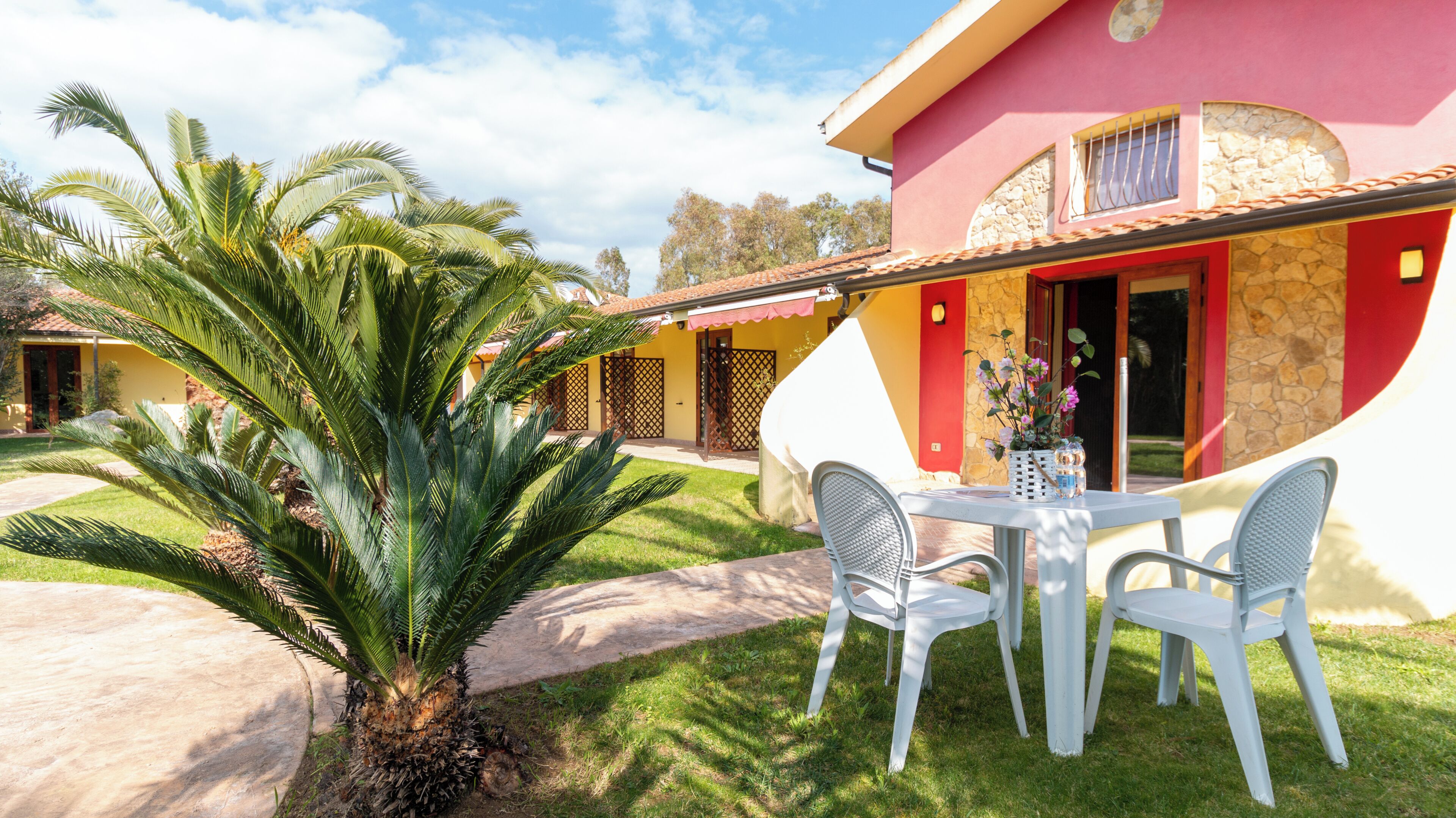 A house with a patio, a palm tree, and a table with chairs.