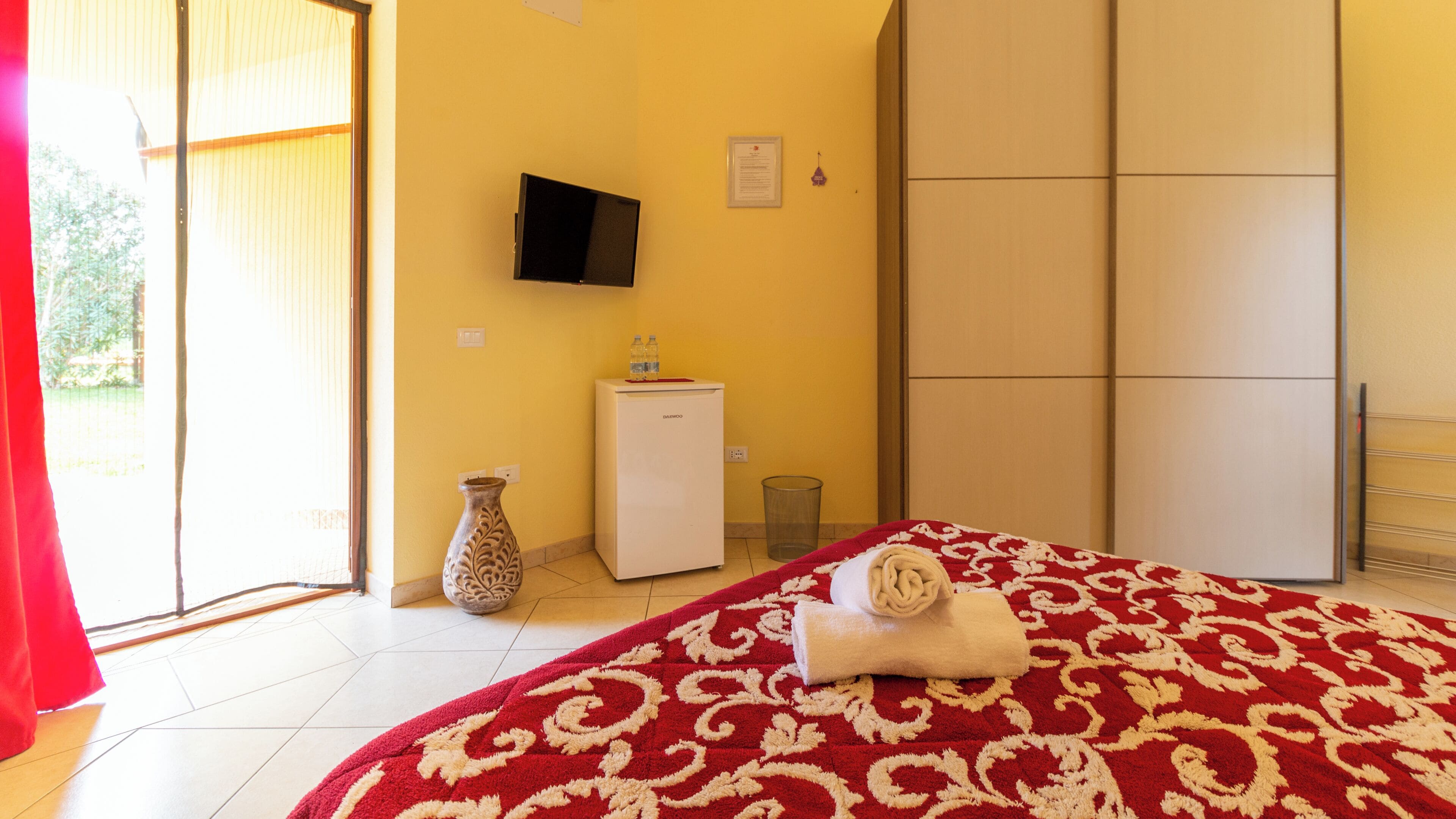 Une chambre d’hôtel comprenant un lit, une télévision, un petit bureau, un vase et une armoire.