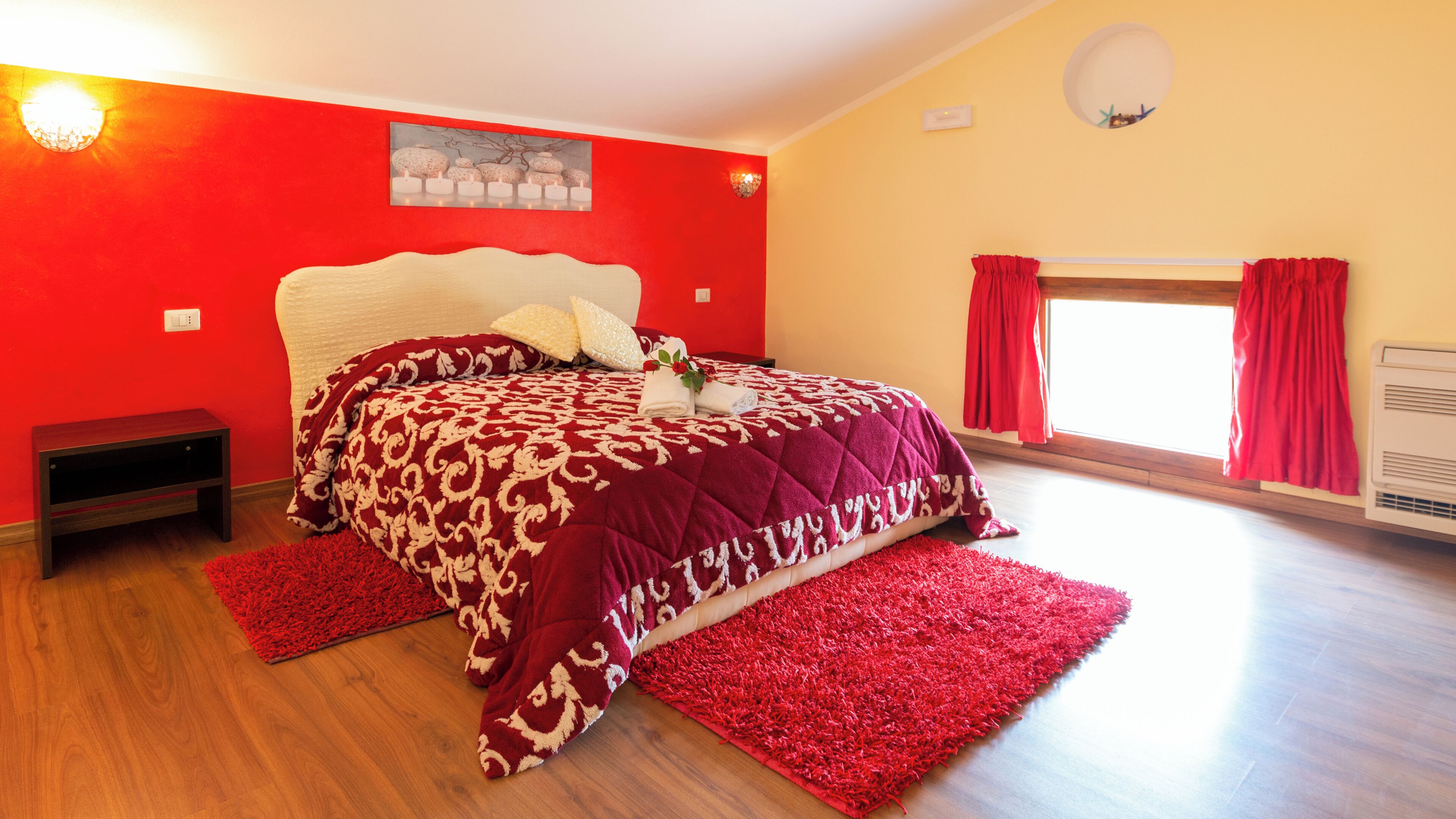 Un dormitorio con una cama grande, una pared roja y una ventana con cortinas.