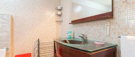 A bathroom with a glass sink, a wooden vanity, a red stool, and a tiled wall.