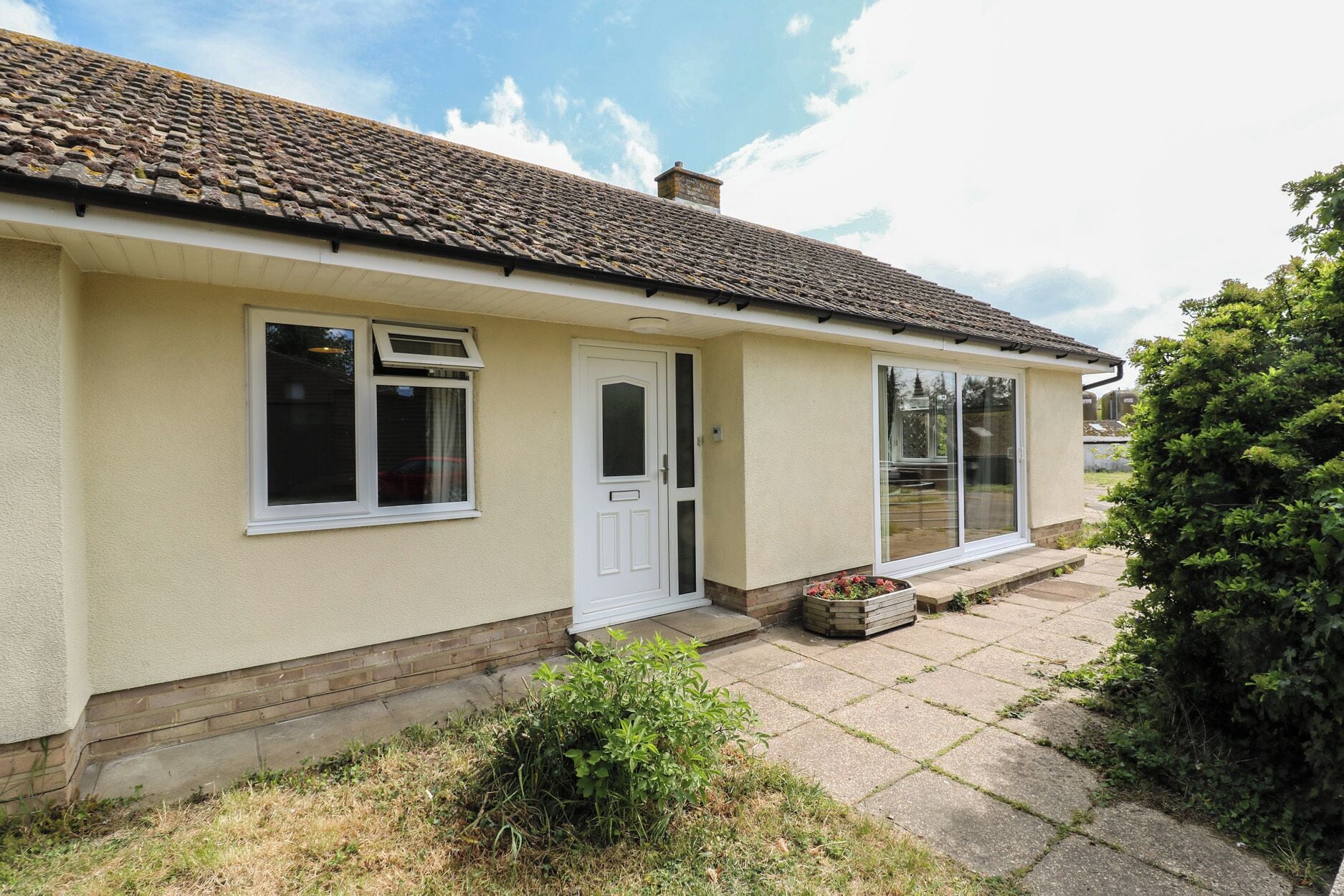 Une maison de plain-pied avec un toit en tuiles, une porte d’entrée et une porte-fenêtre coulissante.