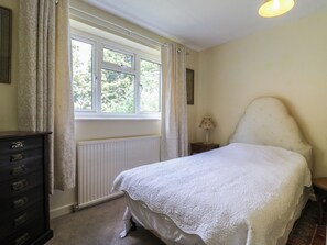 A bedroom with a bed, a dresser, a window with curtains, a radiator, and a lamp. - The Lodge (Colchester)