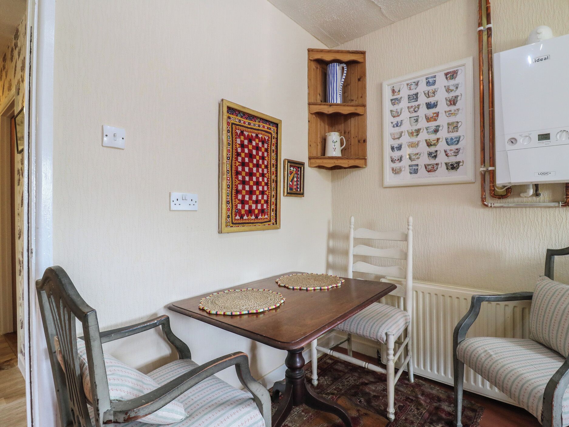 A dining area with a wooden table, two chairs, a shelf with a teapot, and a framed tea set.