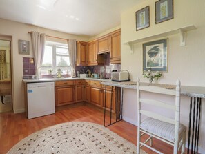 A kitchen with wooden cabinets, a dishwasher, a toaster, and a white chair. - The Lodge (Colchester)