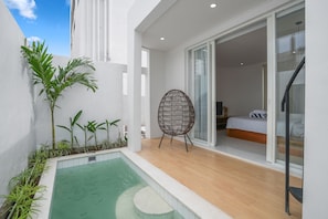 A modern bedroom with a bed, a wicker chair, and a small pool area with plants. - New Rooftop Jacuzzi & Private Pool Villa near Canggu/Seminyak. (Bali)