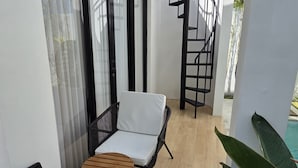 A balcony with two wicker chairs, a small wooden table, and a black spiral staircase leading to an upper level. - New Rooftop Jacuzzi & Private Pool Villa near Canggu/Seminyak. (Bali)