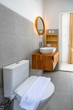 A bathroom with a toilet, sink, wooden vanity, mirror, and a towel on the seat. - New Rooftop Jacuzzi & Private Pool Villa near Canggu/Seminyak. (Bali)