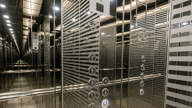 Et moderne elevatorinteriør med spejle i glas og metaldetaljer, der viser et skilt med angivelse af en passager-elevatorkapacitet på 630 kg for 8 personer.