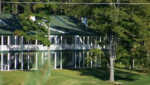 A large, two-story building with a green roof and white columns, surrounded by lush greenery and a golf course. - Fairway to Heaven II at Shanty Creek (Bellaire)