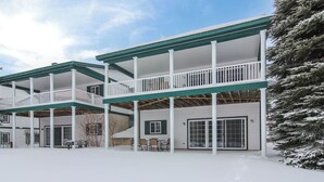 A multi-story building with a covered patio area, large windows, and a snow-covered ground. - Fairway to Heaven II at Shanty Creek (Bellaire)