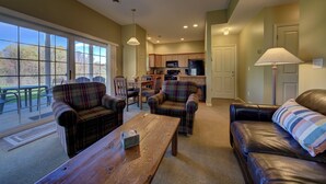 A living room with a wooden coffee table, plaid sofas, and a view of the backyard through large windows. - Fairway to Heaven II at Shanty Creek (Bellaire)