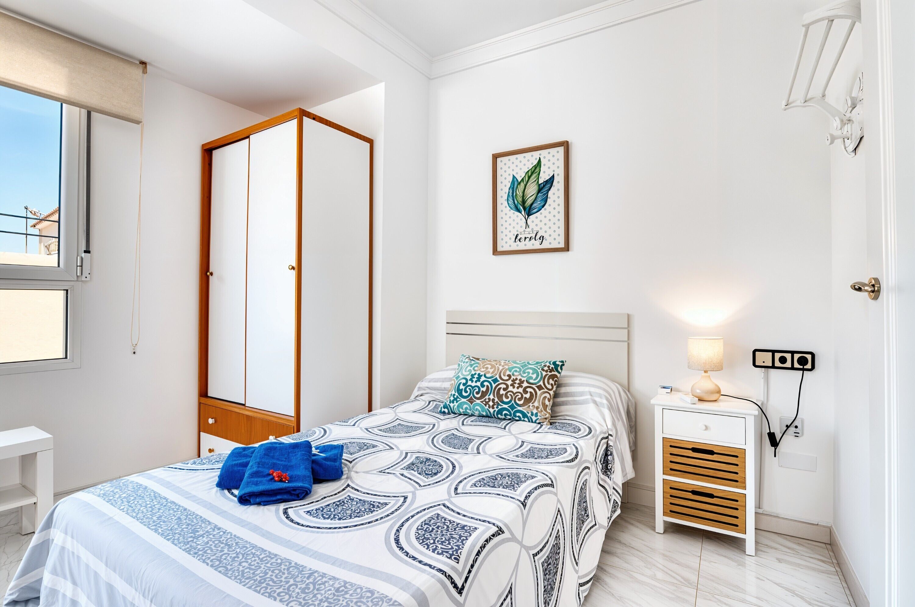 Quarto com cama, mesa de cabeceira, luminária na parede, obra de arte emoldurada e guarda-roupa.