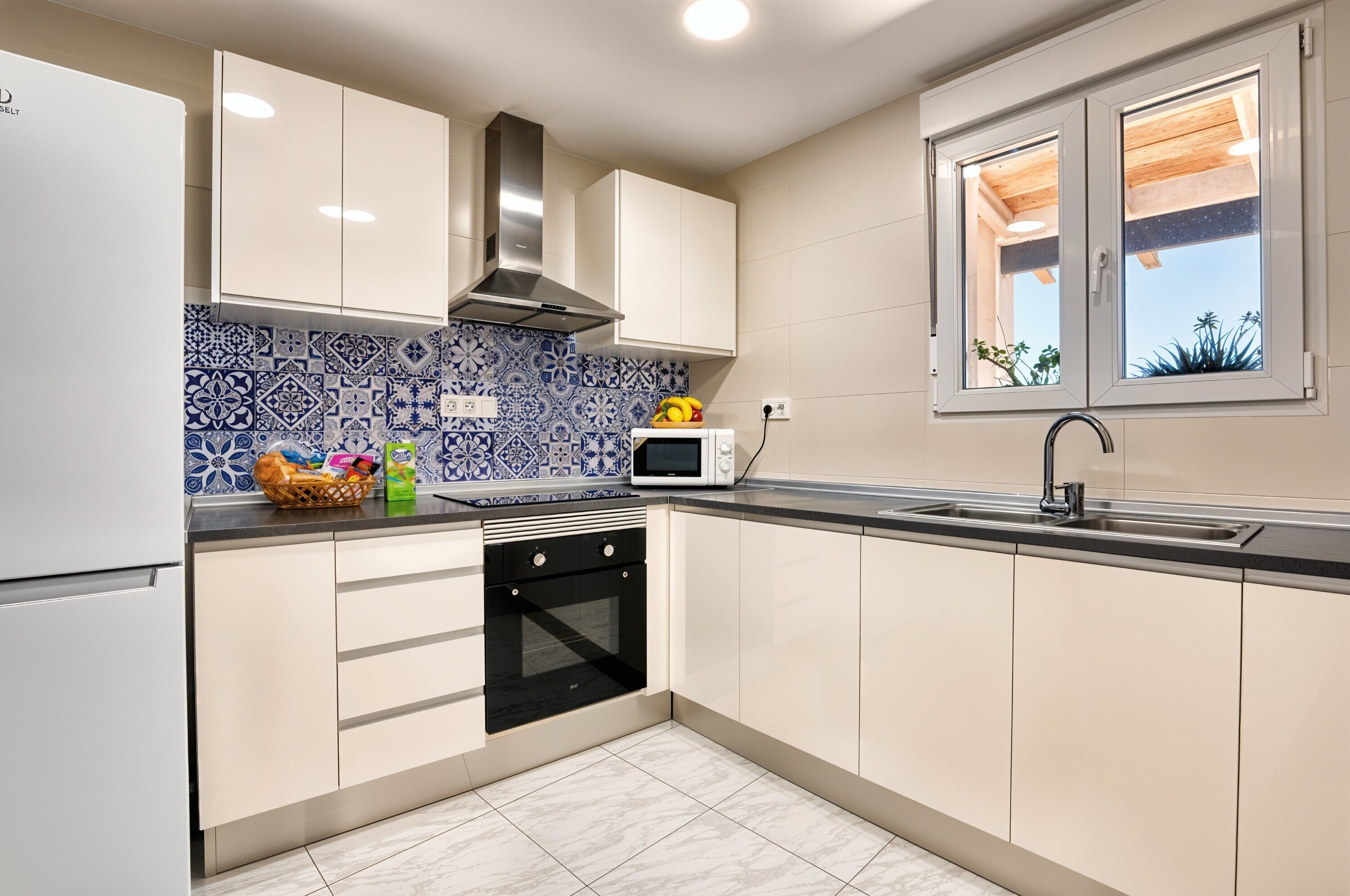 Una cocina moderna con armarios blancos, horno integrado, microondas y ventana con vistas al cielo.