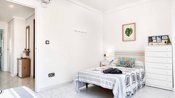 A bedroom with a bed, bedside table, dresser, and a wall-mounted shelf with framed pictures.