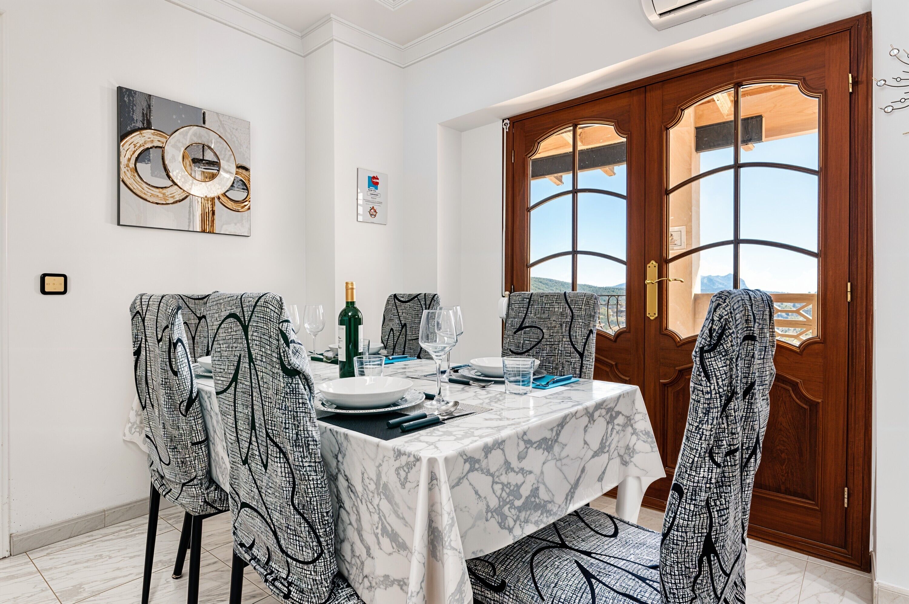 Uma área de refeições com uma mesa de mármore, cadeiras estampadas e vista através de uma porta de madeira.