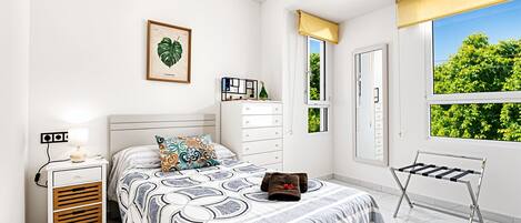 A bedroom with a bed, a nightstand, a dresser, a window with a view, and a radiator.