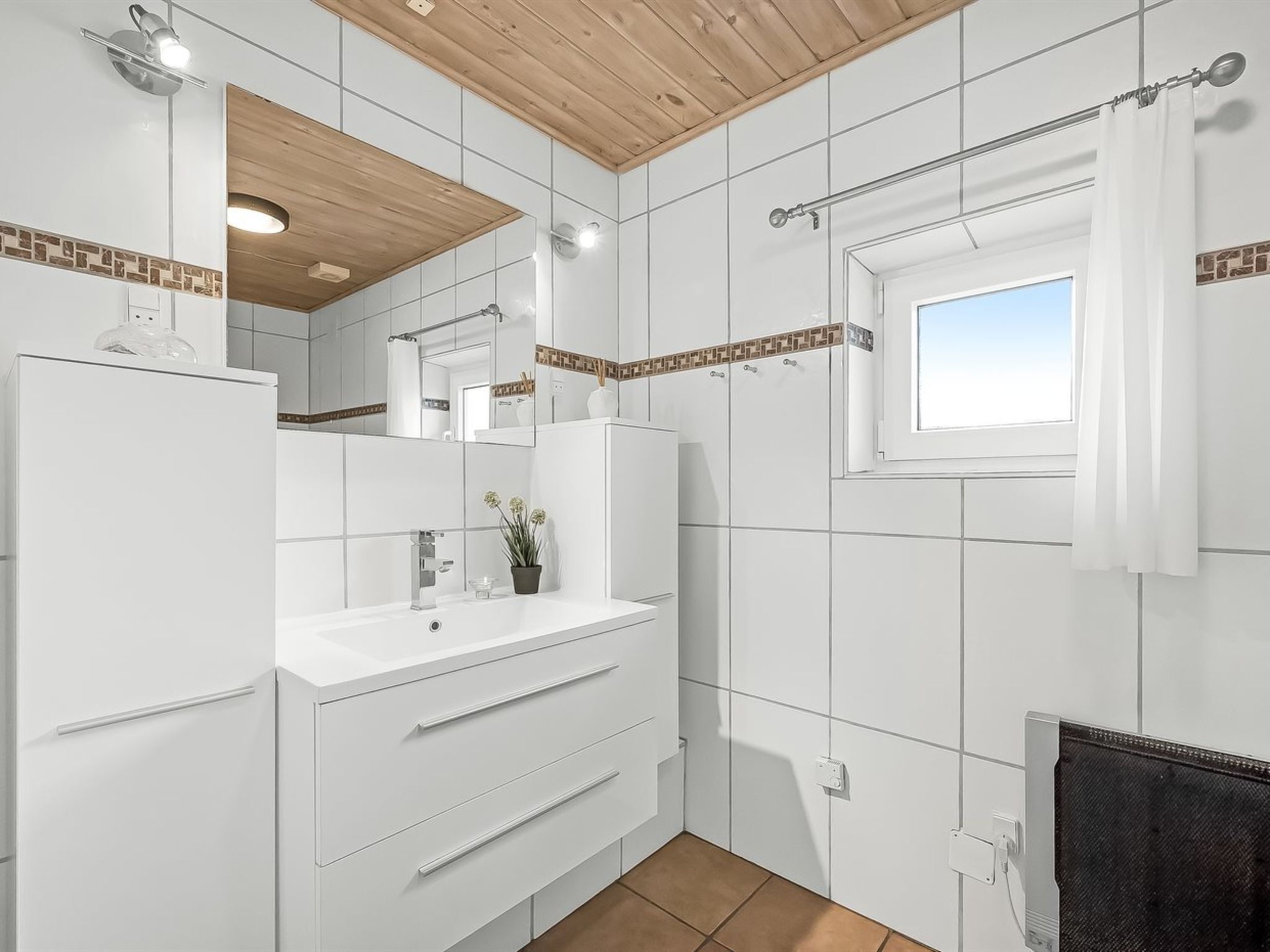 Un baño moderno con baldosas blancas, techo de madera, ventana y zona de ducha.