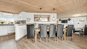 Een moderne keuken en eetruimte met houten vloeren, witte kasten en een groot eiland met zitplaatsen.