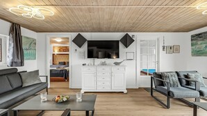 Een moderne woonkamer met een houten plafond, een flatscreen televisie, witte kasten en een eethoek.