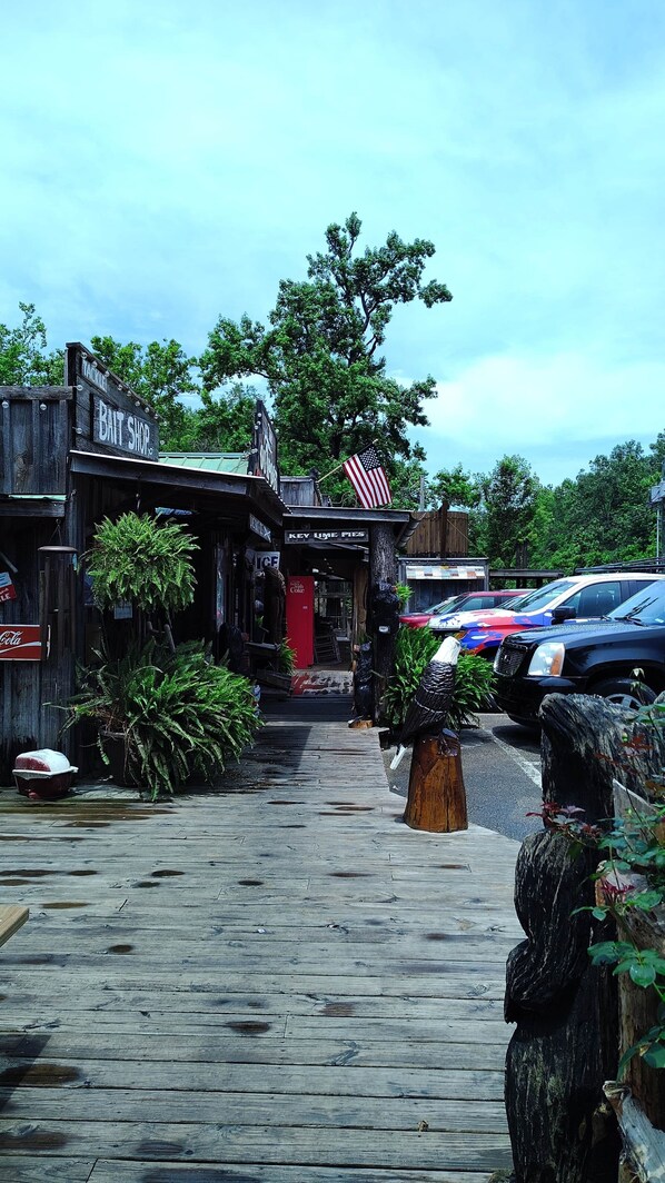 A wooden boardwalk leading to a rustic building with a sign for a bait shop and a pizzeria.