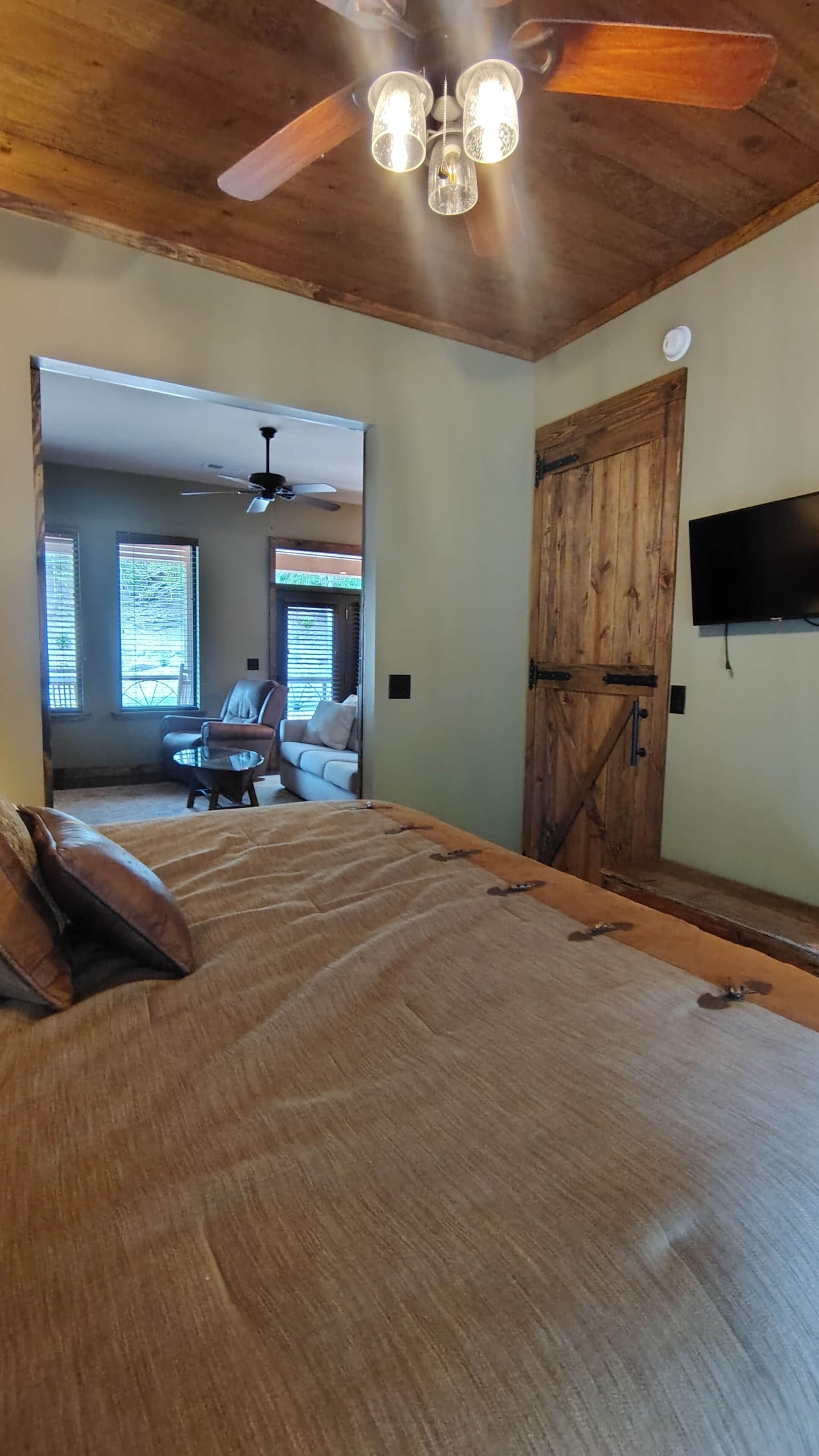 Une chambre avec un grand lit, un ventilateur de plafond, une armoire en bois et un téléviseur fixé au mur.