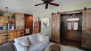 A rustic interior with a sofa, wooden cabinets, a kitchen area, and a sliding barn door. - Prospector Pickwick Lake / Presidential Suite (Hardin County)