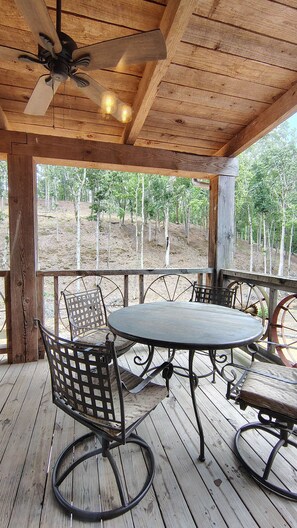 A wooden deck with a round table and metal chairs, a ceiling fan, and a view of trees. - Prospector Pickwick Lake / Presidential Suite (Hardin County)