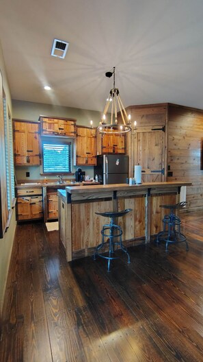 A kitchen with wooden cabinets, a central island with stools, a chandelier, and a built-in refrigerator.