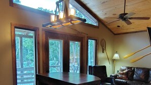 Un interior de madera con una mesa de comedor, un ventilador de techo y ventanas grandes.