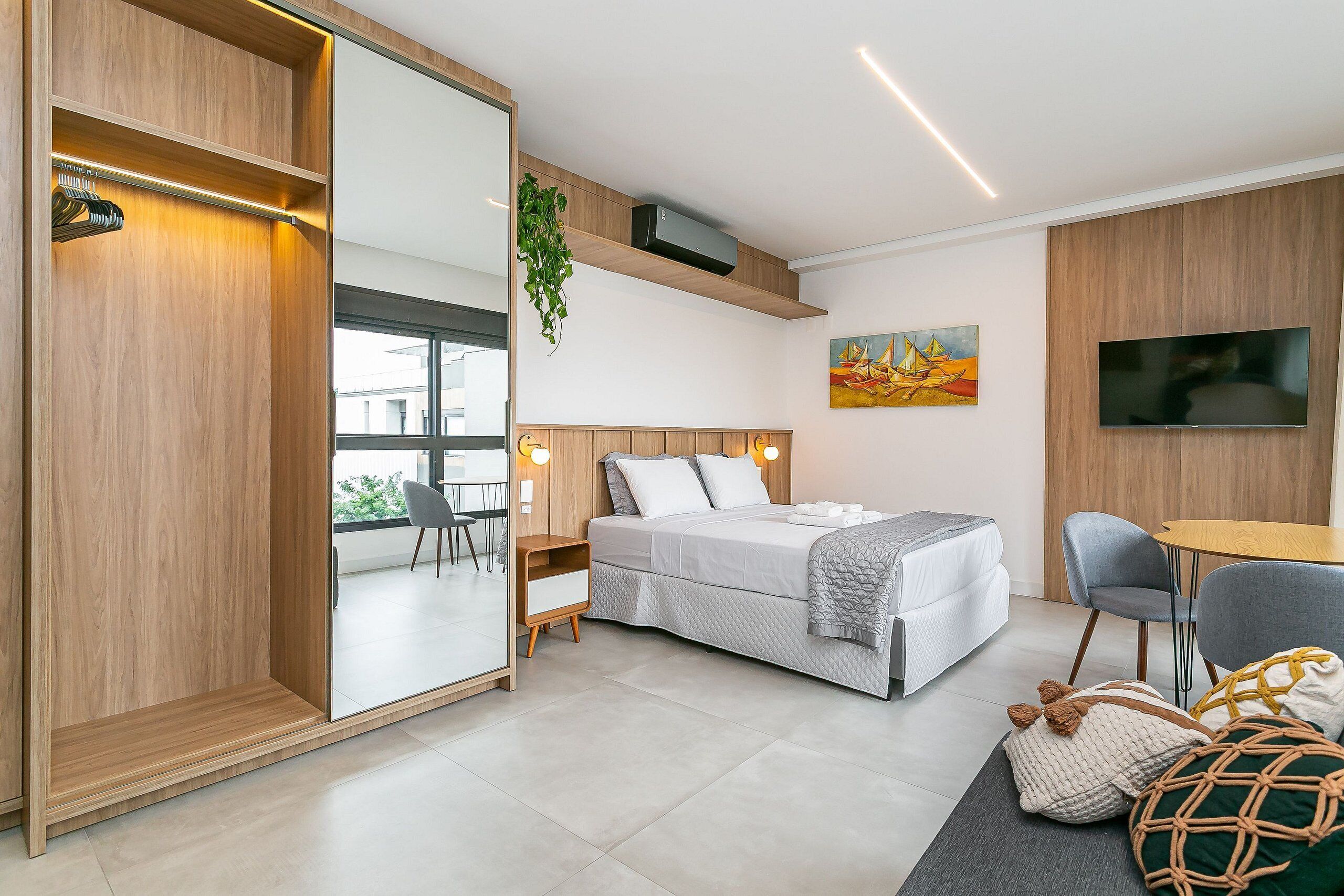 Un dormitorio moderno con cama, mesita de noche, silla, televisor y un ventanal grande.