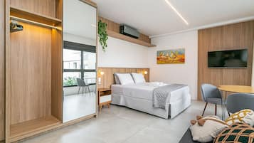 Un dormitorio moderno con cama, mesita de noche, silla, televisor y un ventanal grande.